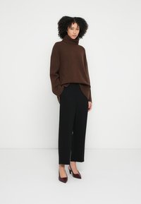 Pulover cu guler înalt maro din tricot moale, asortat cu pantaloni negri evazați, cu talie înaltă, și pantofi burgundy cu vârf ascuțit.