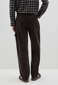 Bruine corduroy broek met een losse pasvorm, voorzien van twee achterzakken en een zijcargozak, gecombineerd met donkere schoenen en een geruit overhemd.