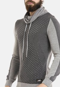 Grauer Pullover mit strukturiertem Muster und gestreiftem Design. Verfügt über einen Schalkragen und Kordelzug. Aus Strickstoff, schmal geschnitten.