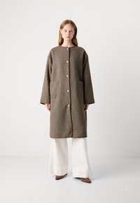 Brun, teksturert frakk med rett silhuett, med knappeåpning, to frontlommer og beige piping ved kantene.