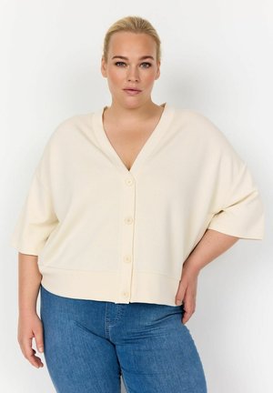 Cardigan oversize color crema con scollo a V, maniche corte e cinque bottoni sul davanti. Tessuto morbido e liscio con vestibilità rilassata.