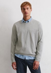 Lichtgrijze sweatshirt met ronde halslijn, geribde manchetten en zoom, gelaagd over een blauwe overhemd met kraag, gedragen met marineblauwe broek. Gelaagde textuur.