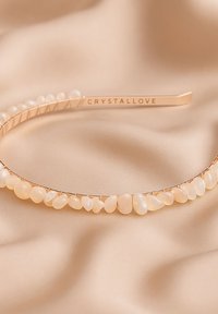 Różowe złoto opaska do włosów z nieregularnie ukształtowanymi jasnymi kamieniami, umieszczonymi wzdłuż cienkiego, teksturowanego drutu. Na opasce wygrawerowano napis "CRYSTALLOVE".