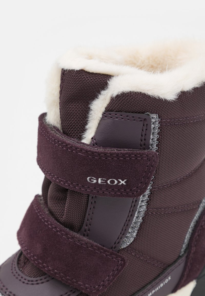 Lila wasserdichte Stiefel mit Klettverschlussriemen, Fellfutter am oberen Rand, geprägtem Logo und strukturierten Materialien für besseren Grip und Komfort.