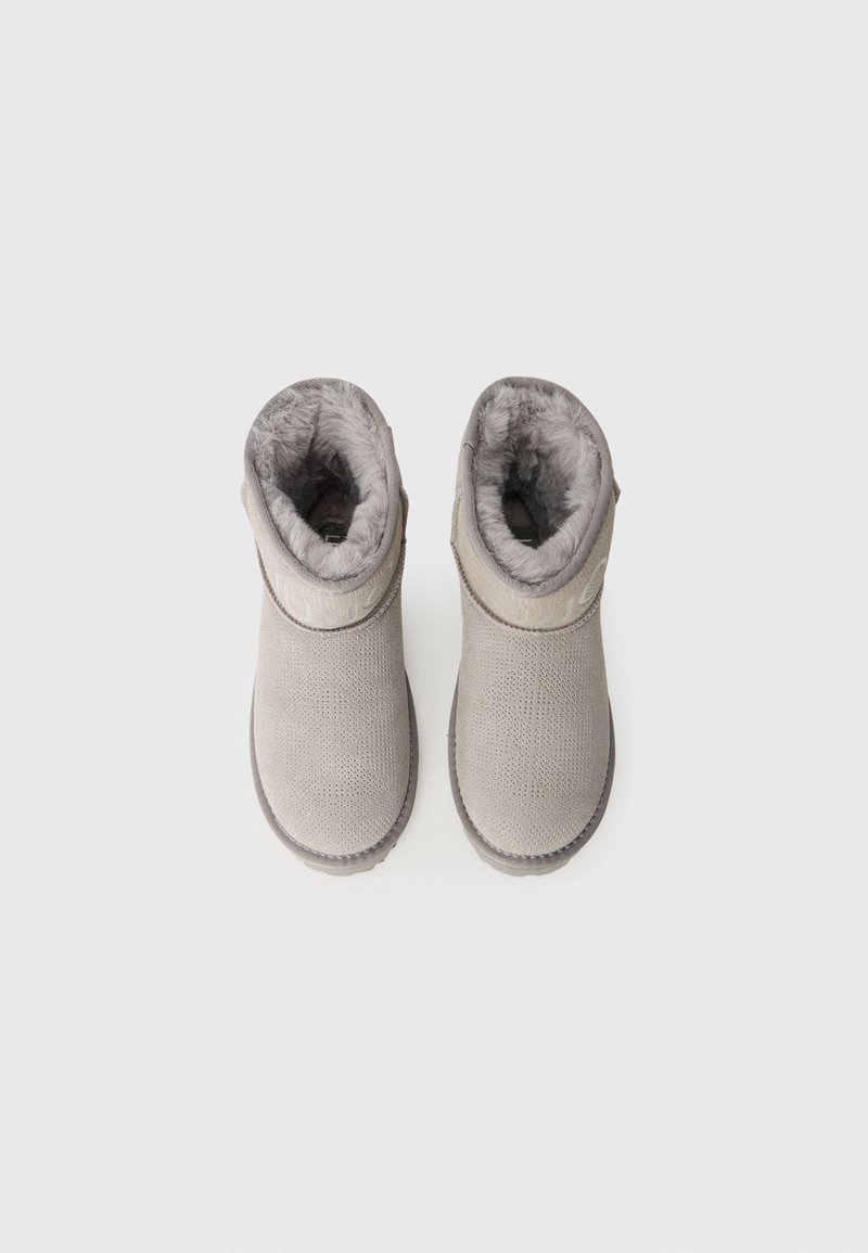 Bottines gris en cuir texturé, doublure en fourrure douce et détail de logo circulaire. Semelles plates avec un motif de traction léger.