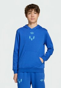 Sweatshirt azul feita de mistura de algodão, com bolso frontal, punhos canelados e logótipo em relevo. Combinada com calças de fato de treino azuis correspondentes.