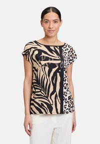 T-shirt à manches courtes présentant un mélange d'imprimés zèbre et léopard en noir, beige et marron, orné de clous décoratifs sur le devant.