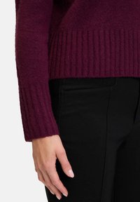 Pull à côtes bourgogne avec une texture douce, doté de manches longues et d'une coupe décontractée, associé à un pantalon noir bien ajusté.