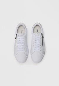 Hvite sneakers laget av glatt syntetisk materiale, med snøring og sideskJermer. Har en grå akseNn på hælen og sømdetaljer.