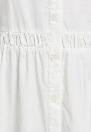 Biela košeľa s gombíkmi s textúrovaným telom a zviazaním, piatimi gombíkmi a hladkým povrchom látky.