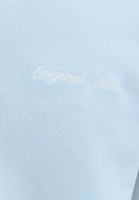 Svetlomodrý textúrovaný materiál s jemným bielym vyšitým kurzívnym textom "Dsquared2 Studio."