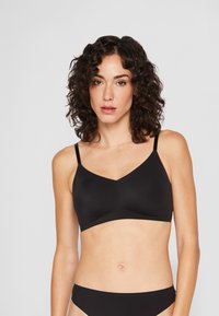 Mustat langattomat bralette-rintaliivit V-mallisella kaula-aukolla, säädettävillä olkaimilla ja sileällä pinnalla. Ominaisuuksiin kuuluu minimalistic design ilman näkyvää metalliosaa.