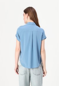 Light blue short-sleeve blouse with a collar, smooth texture, relaxed fit, back pleat detail, and a rounded hemline.