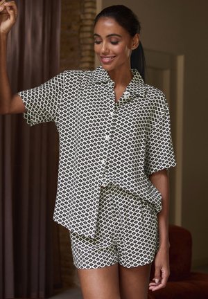 Kurzärmliges, kragenloses Schlafanzug-Set in schwarz-weißem geometrischen Muster, bestehend aus einem Hemd mit Knopfleiste und passenden Shorts. Glatte Stofftextur.