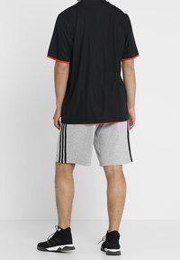 Svart idrottströja med röda detaljer, grå shorts med svarta sidostråk, kombinerat med svarta idrottsskor. Synlig bakvy.