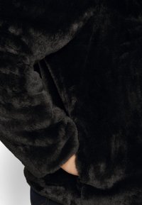 Sort faux fur-jakke med en blød, luksuriøs tekstur, runde ærmer og en sidelomme for praktisk anvendelse.