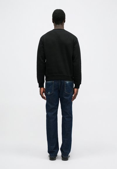 Zwarte sweatshirt met ronde hals, gecombineerd met blauwe denim jeans met achterzakken. Het ontwerp is eenvoudig met een relaxte pasvorm.
