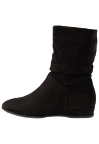 Černé kotníkové boty z semiše s volnou horní částí, špičatou špičkou a nízkým klínovým podpatkem, s hladkou texturou a minimalistickým designem.
