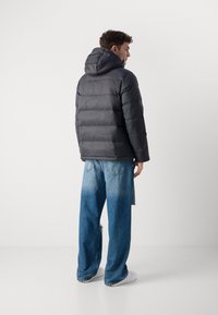 Grijze gewatteerde jas met een capuchon, voorzien van horizontale stiknaden. Gecombineerd met lichtblauwe wijde denim jeans en witte sneakers.