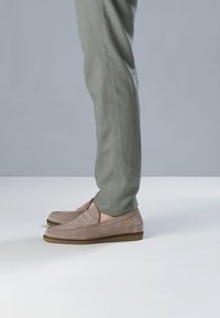 Beige loafers van suède, met een rubberen zool en gestikte details. Gecombineerd met lichtgroene, op maat gemaakte broeken.