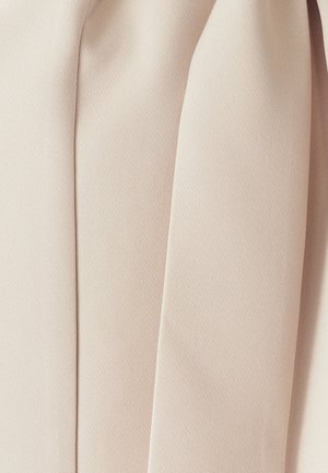 Gaisā bežā audumā ir gluda, strukturēta virsma, kas rāda vairākus salocījumus un kroku, nodrošinot niansētu drapējuma efektu.