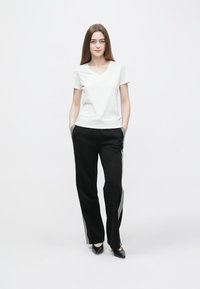 White v-neck t-shirt paired with black pants featuring side stripes. The fabric appears soft; the pants have a relaxed fit and pockets.