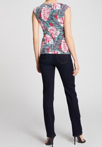 Blomstret top med korte ærmer i pink og grøn på en hvid baggrund, parret med mørkeblå lige ben jeans og sorte hæle.