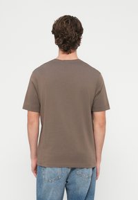 Rjava bombažna majica s kratkimi rokavi, okroglim izrezom in sproščenim krojem, kombinirana s svetlo modrimi denim hlačami. Enostavna zasnova v gladki barvi.