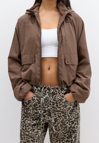 Brown, lightweight jacket with a zip front, two flap pockets, and adjustable hood, paired with tapered leopard print pants.