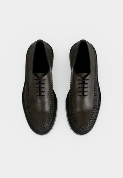 Ζευγάρι μαύρα δερμάτινα επίσημα παπούτσια με πλεχτές λεπτομέρειες και κλειστό κορδόνι, εμφανίζεται από πάνω σε λευκό φόντο.