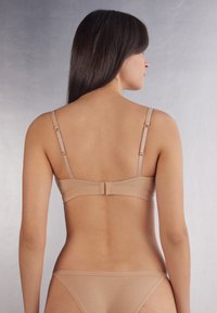 Nude bra with adjustable straps, a seamless design, and a clasp back. Smooth texture with no visible embellishments or patterns.