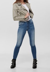 Lys grå faux læder bikerjakke, tætsiddende hvid skjorte, blå skinny jeans og sorte ankelstøvler med spænde detaljer.