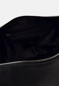 Svart läderbag inuti med slät textur, med en blixtlåsficka och en etikett präglad med "Tiger of Sweden."