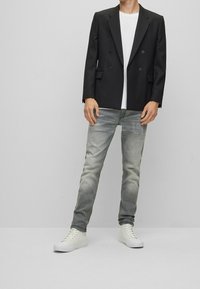 Blazer negro de corte cruzado sobre una camiseta blanca, combinado con jeans skinny gris claro y zapatillas altas blancas. Tejidos suaves, corte moderno.