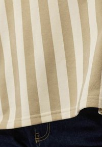 Tissu à rayures verticales beige et blanc suspendu au-dessus d'un denim bleu foncé avec des coutures jaunes.