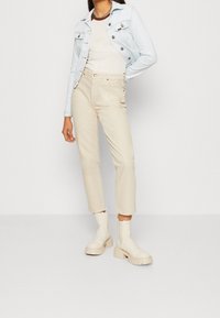 Světlá denimová bunda se stříbrnými knoflíky, bílým tričkem, béžovými kalhotami s vysokým pasem a béžovými robustními kotníkovými botami s hladkým povrchem.