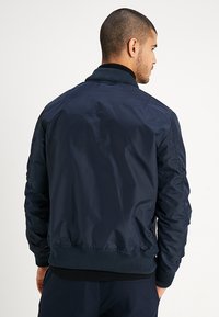 Chaqueta bomber azul marino hecha de un tejido suave y ligero. Presenta un cuello y puños acanalados, con una parte trasera estructurada y acentos cosidos.