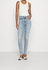 Ljust blå, slim-fit jeans med en blekt tvätt, som har fem fickor och en knappstängning, kombinerat med en vit ärmlös topp och svarta klackar.