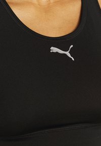 Svart sport-bh av mjukt, stretchigt tyg. Har en rundad halsringning och en vit Puma-logotyp på vänster sida.