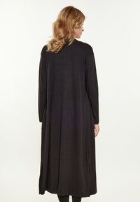 Schwarzes Langarmkleid mit fließendem Design und Schlitzdetails an den Seiten, aus einem weichen, leichten Stoff gefertigt.