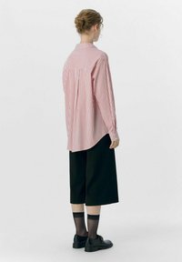 Rød og hvid stribet oversized skjorte lavet af bomuld, med en rygklap. Sammen med løse sorte culottes og sorte sko.