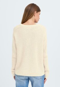 Strikkegenser i kremet beige, med vid halslinning, ribbestrikkede mansjetter og en avslappet passform. Teksturert stoff med åpen veving.