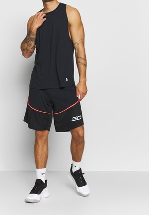 Homme portant un débardeur de sport noir, un short de basket-ball noir avec une bordure rouge et un logo "30" blanc, des chaussettes blanches et des baskets noires et blanches.