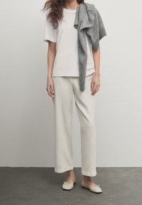 Witte t-shirt met korte mouwen gecombineerd met lichtbeige wijde broek. Een grijze gebreide trui over de schouders gedrapeerd. Beige flats maken de outfit compleet.