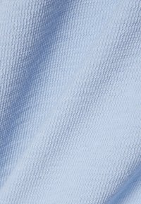 Vaaleansinistä kudottua kangasta, jossa on kohokuvioitu vohvelikuvio ja pinnalla näkyy pehmeitä poimuja.