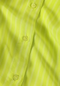 Camisa amarilla neón con rayas blancas estrechas, con botones amarillos y una textura suave, ligeramente brillante.