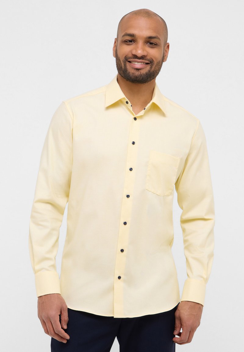 Camicia a maniche lunghe di un leggero giallo con colletto a punte, dotata di taschino sul petto e dettagli con bottoni scuri. Tessuto morbido, vestibilità sagomata.
