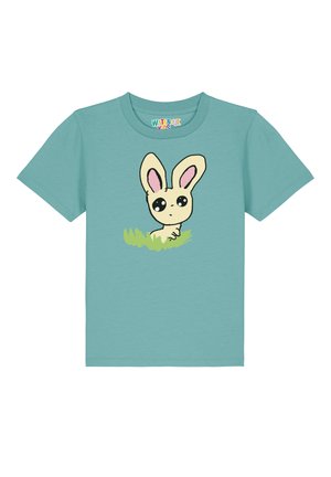 Hellblaues T-Shirt mit kurzen Ärmeln, das einen Cartoon-Hasen mit großen Augen und rosa Ohren zeigt, vor grünem Gras. Aus Baumwolle.