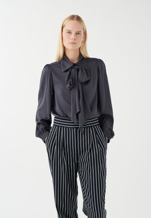 Dunkelgraue Bluse mit einem Schleifenkragen, langen Ärmeln und gepufften Schultern, kombiniert mit marineblauen und weißen gestreiften, hoch taillierten Hosen.