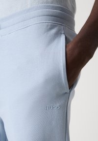 Lys blå joggebukser med en glatt tekstur, som har en ribbet midje, sidelommer og en subtil brodert "HUGO"-logo.
